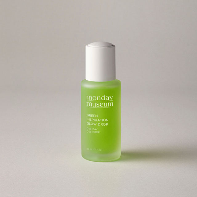 A bottle of 'Monday Museum' green glow drop serum on a plain background.